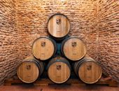 Seis barricas de madera apiladas, dispuestas en forma de pirámide, contra paredes de piedra rústica. Cada barrica lleva estampado un escudo de Bodegas Muñoz