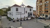 Fachada blanca de la Parroquia El Buen Pastor en Málaga, con el nombre de la iglesia en letras grandes, dos tejados a los lados, una cruz en el centro y un mosaico religioso en la pared principal.